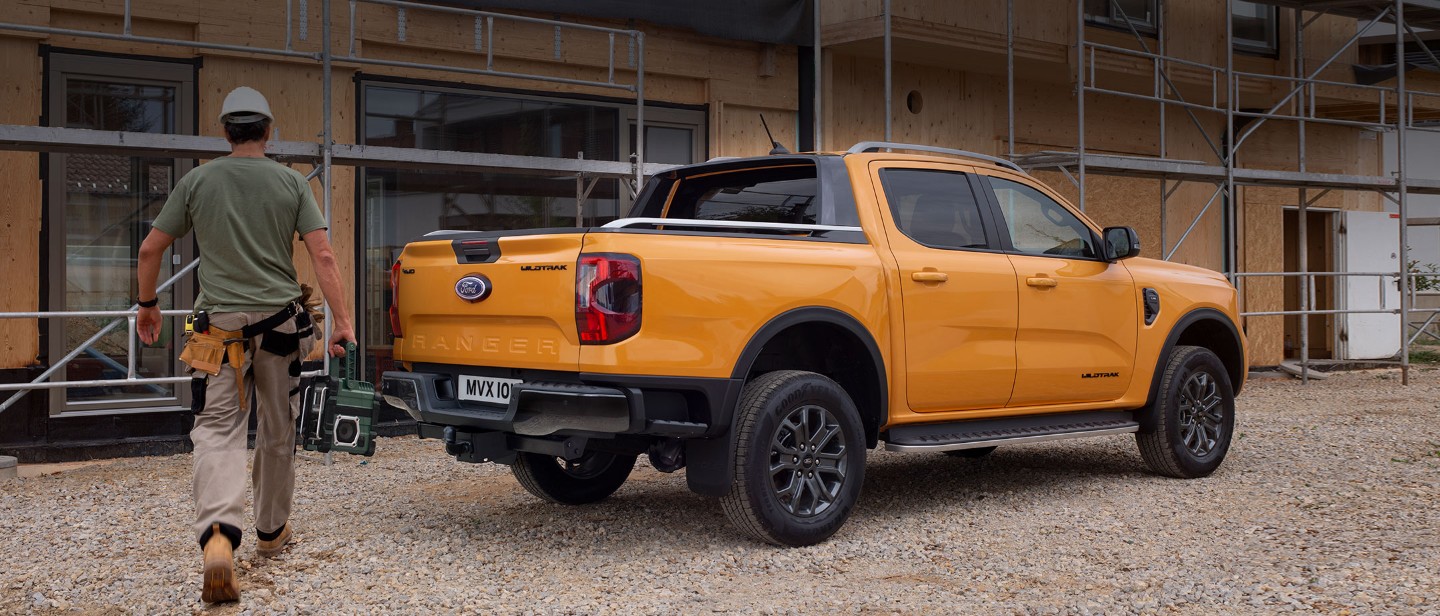 Ford Ranger in Orange. Dreiviertelansicht, parkt vor Wohnhausneubau