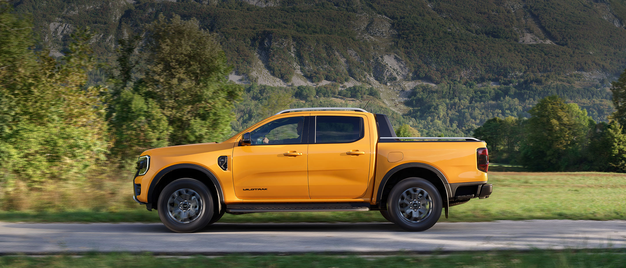 Ford Ranger in Orange. Seitenansicht, fährt durch Gebirgslandschaft