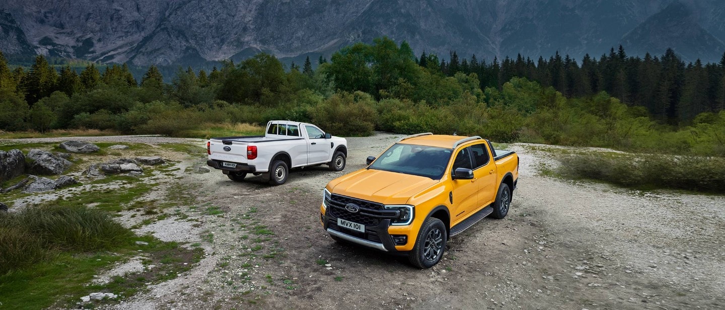 Ford Ranger in Weiß und Orange. Geparkt auf Schotterweg mit Wald und Bergen im Hintergrund