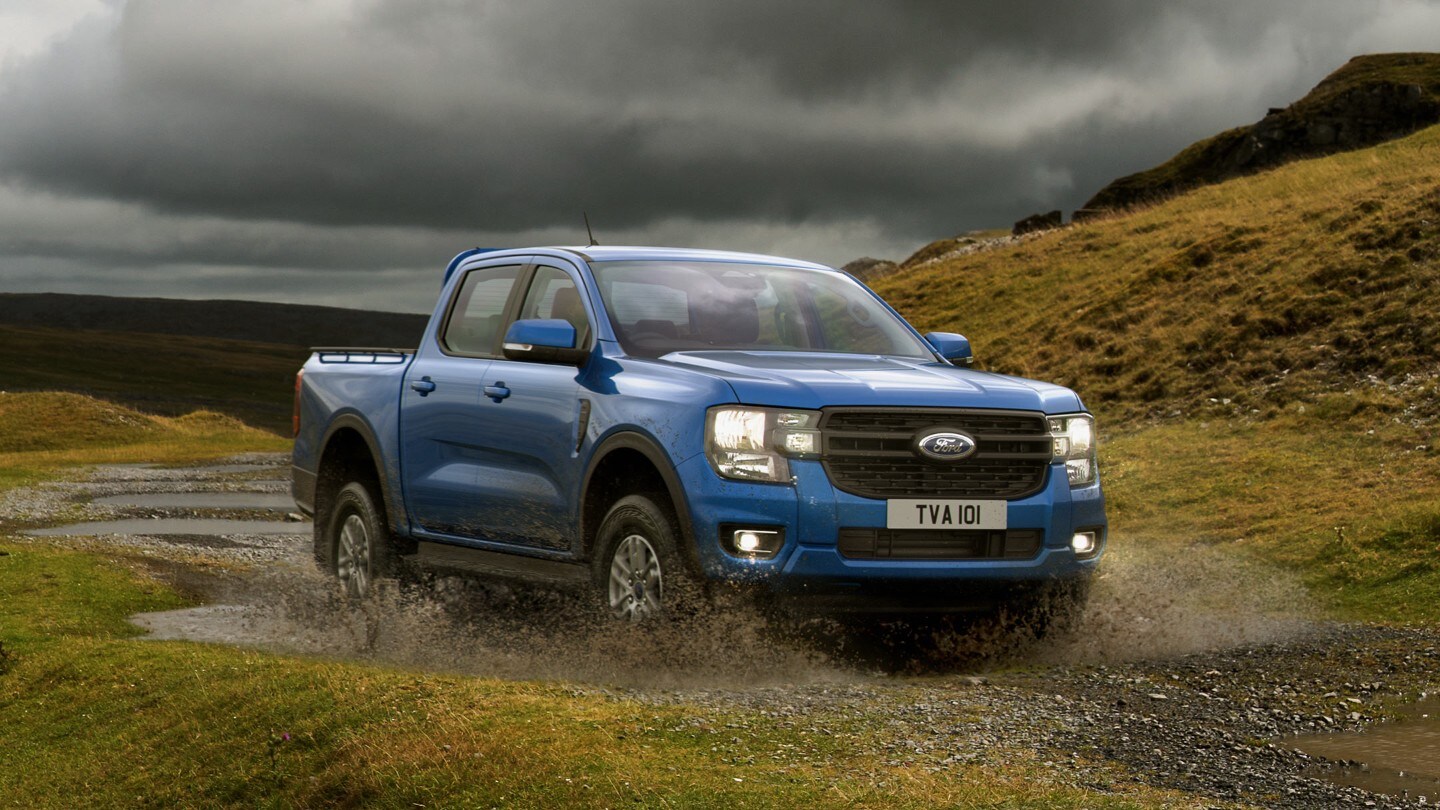 Ford Ranger in Blau. Frontansicht, fährt durch eine Wasserlache in ländlicher Umgebung