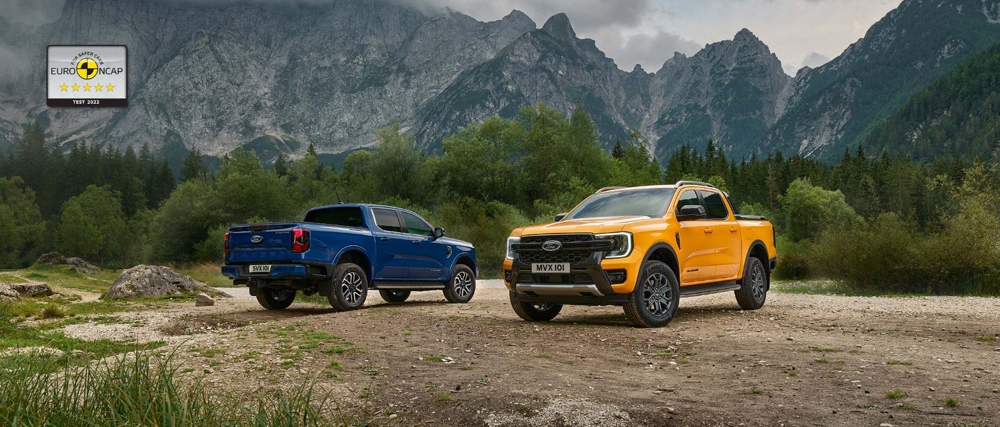 Ford Ranger in Blau und Orange. Geparkt auf Schotterweg mit Wald und Bergen im Hintergrund