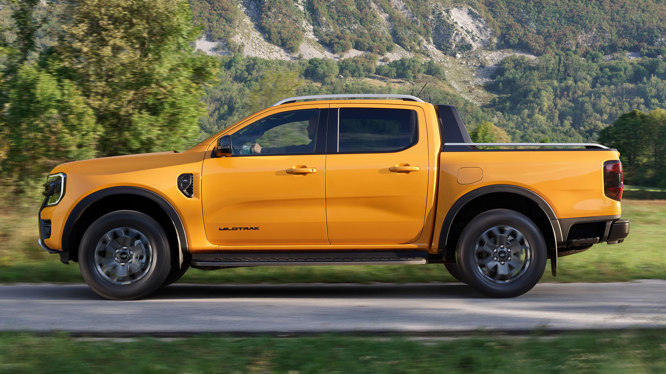 Ford Ranger in Orange. Seitenansicht, fährt durch Gebirgslandschaft