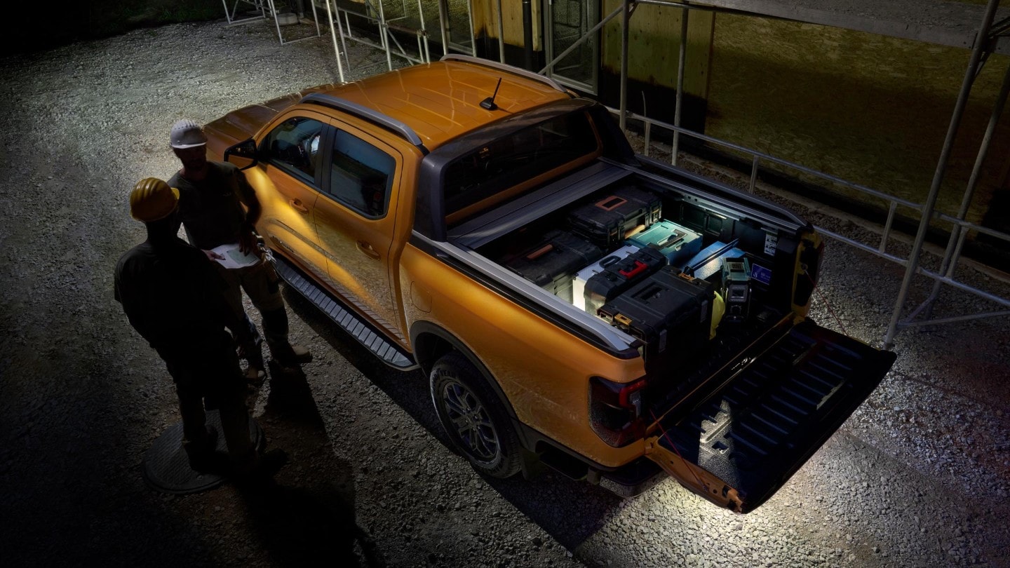 Ford Ranger in Orange. Ansicht von oben, mit beladener Ladefläche parkt bei Dunkelheit vor Wohnhausneubau