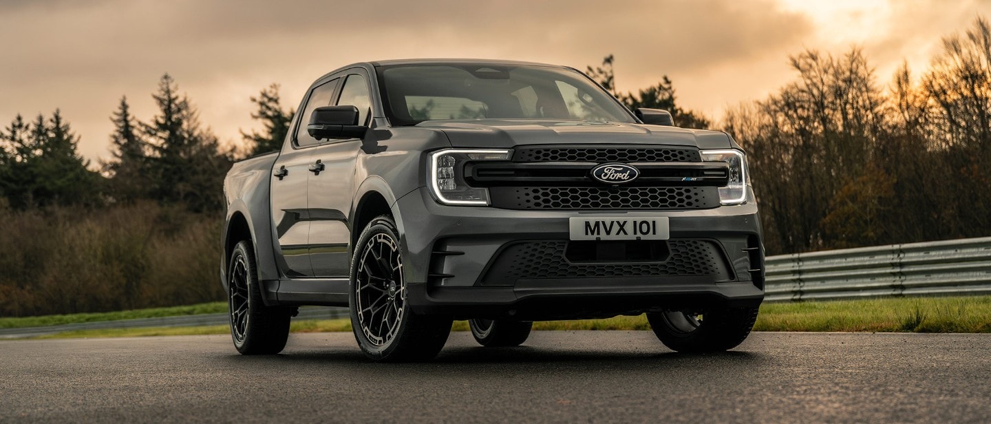 Ford Ranger MS-RT in Grau. Dreiviertelansicht, fahrend auf einer Straße bei Sonnenuntergang.