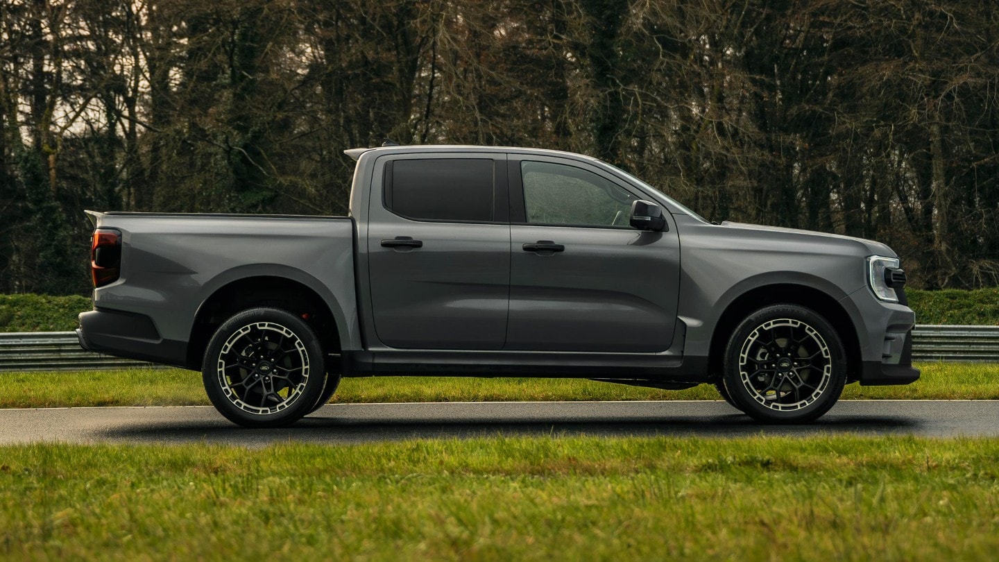 Ford Ranger MS-RT in Grau. Seitenansicht, parkt vor einem Rasen mit Bäumen im Hintergrund.