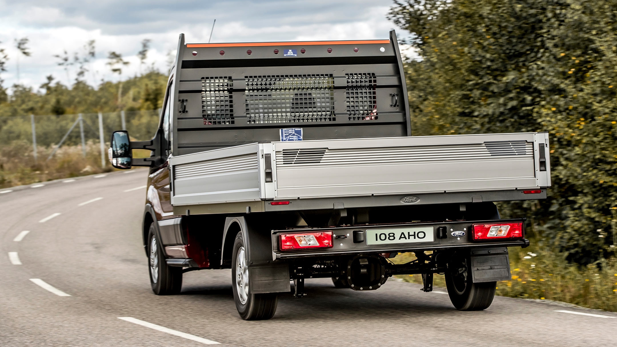 Ford Transit Pritschenwagen Einzelkabine. Heckansicht, fahrend auf einer Landstraße