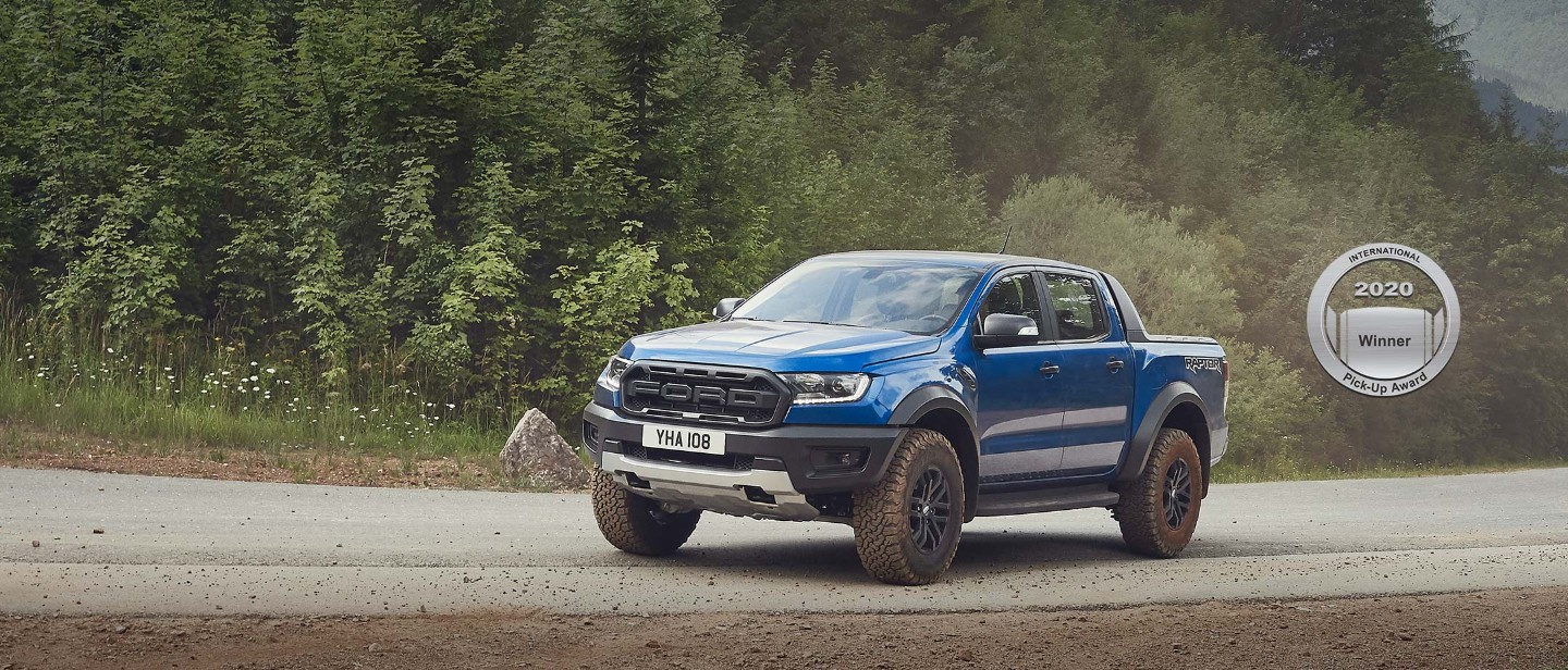 Blue Ford Ranger Raptor driving through a countryside, front three quarter view