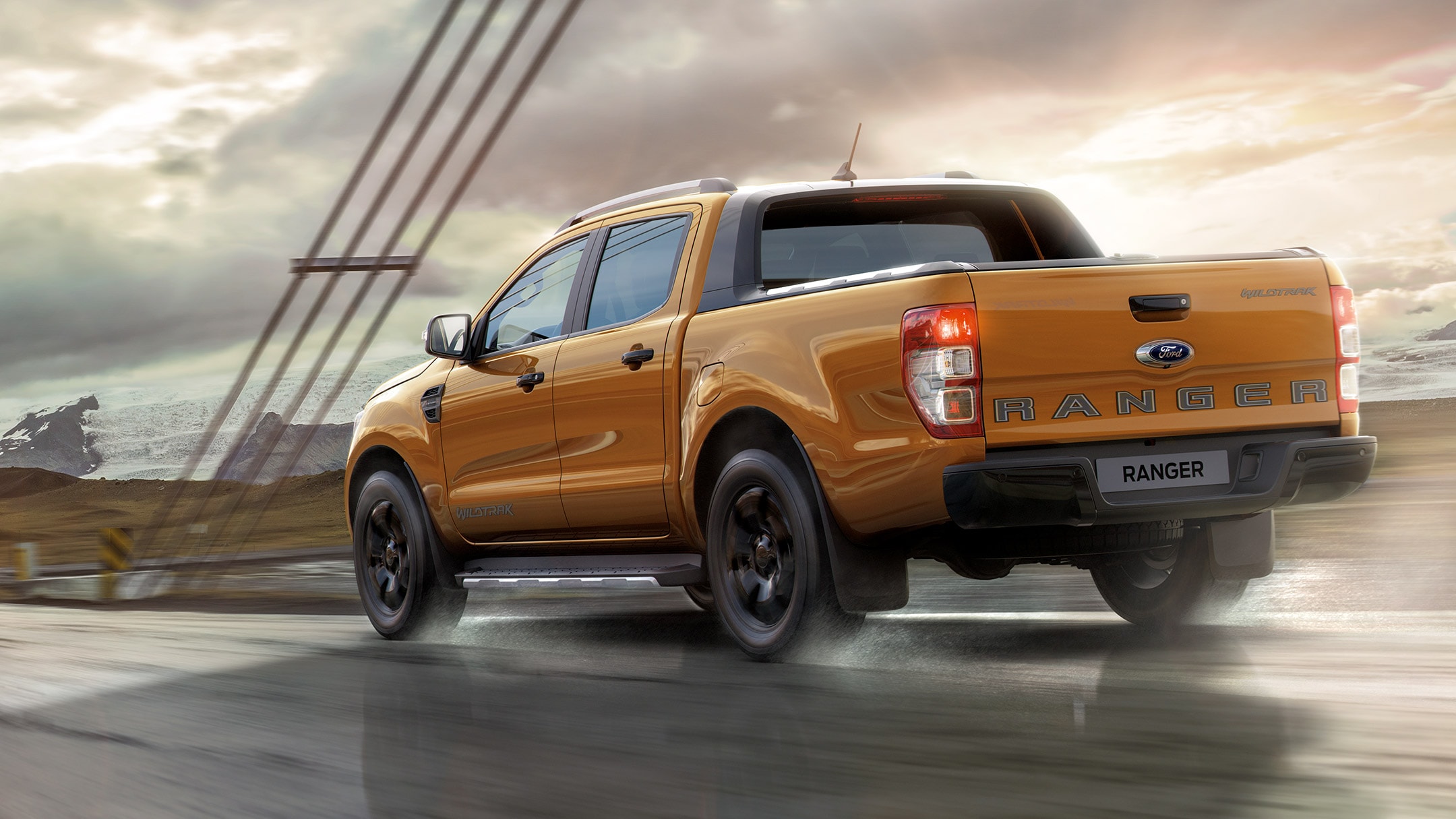 Ford Ranger Wildtrak in Orange. Dreiviertelansicht von hinten, fahrend auf einer Brücke