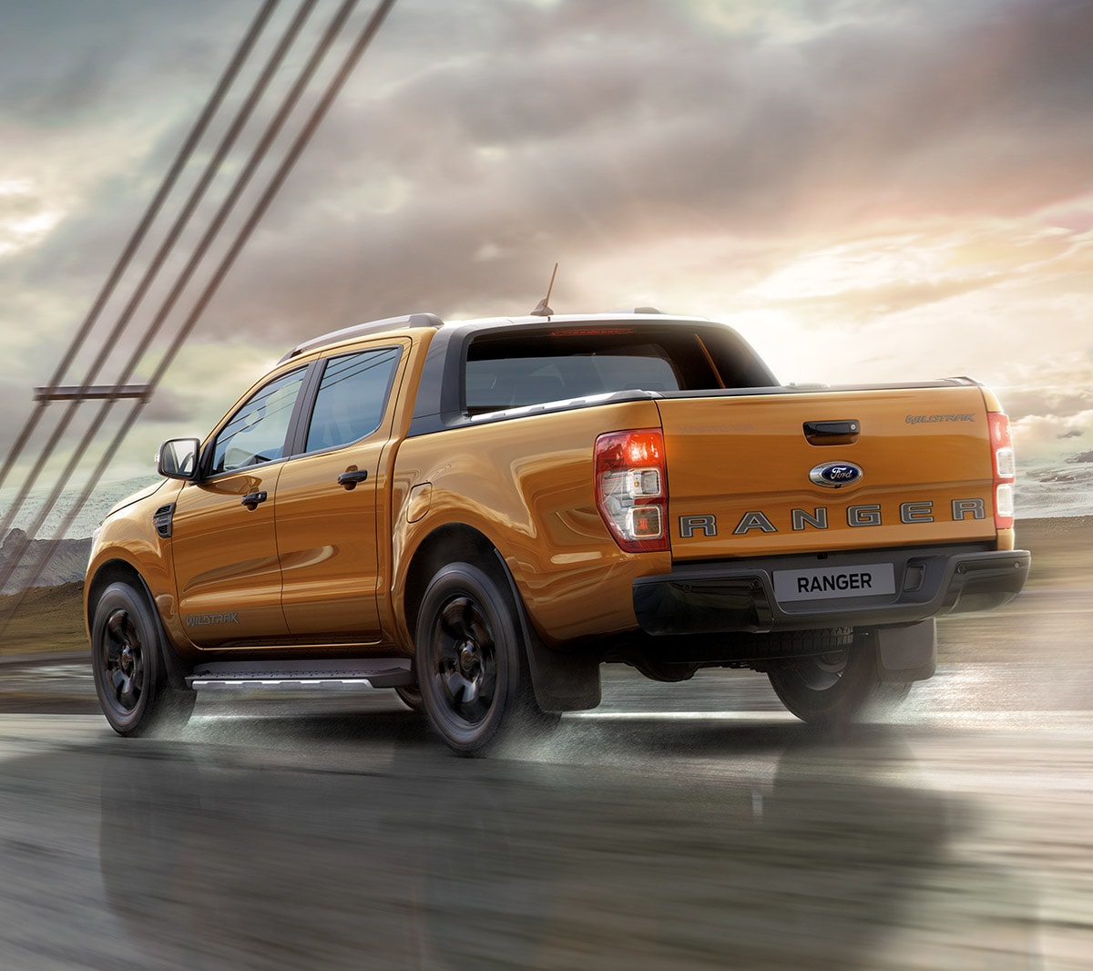 Ford Ranger Wildtrak in Orange. Dreiviertelansicht von hinten, fahrend auf einer Brücke