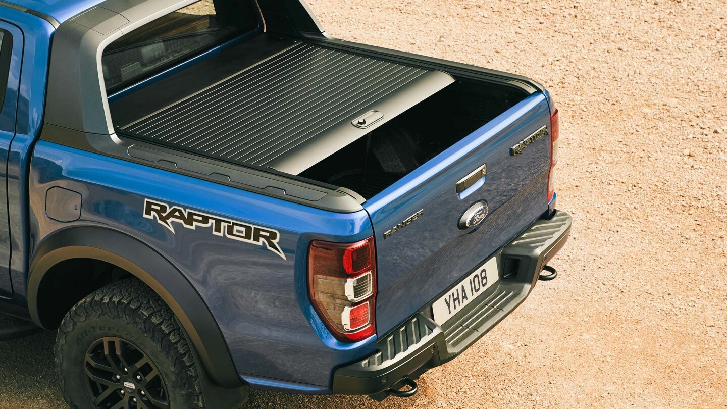 Ford Ranger Raptor in Blau. Dreiviertelansicht von hinten, Ladefläche mit halb geöffneten Laderaumrollo