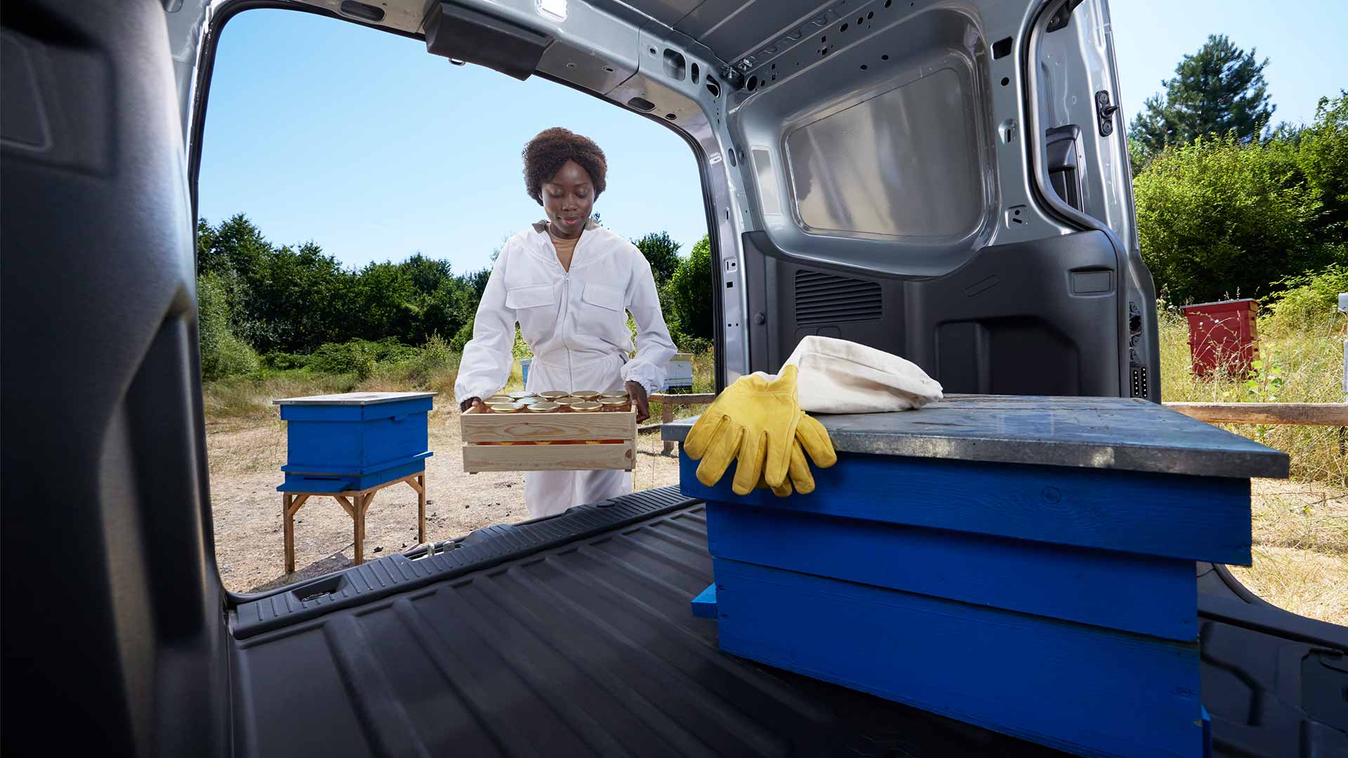 Ford Transit Courier in Silber. Ansicht des Laderaums mit geöffneten Türen, Frau trägt eine Kiste.