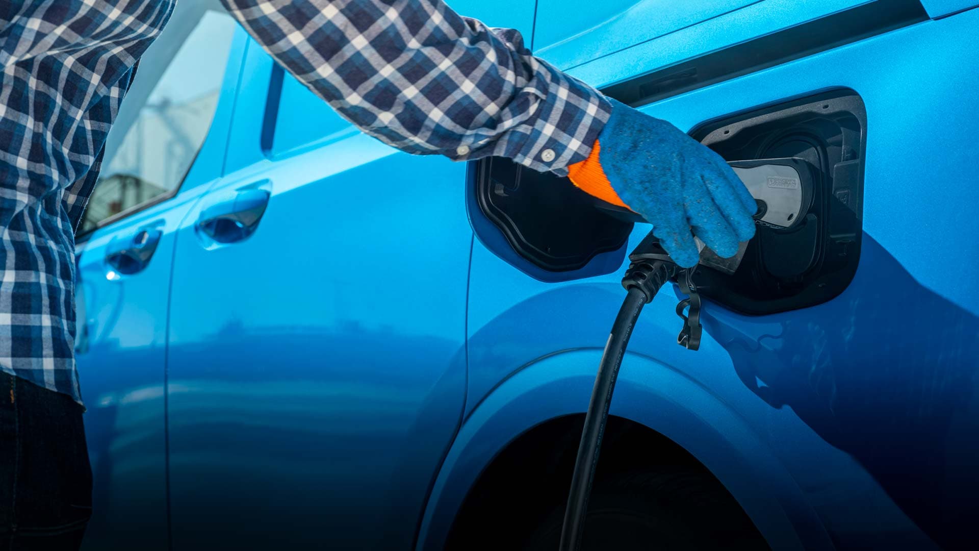 Ford E-Transit Courier in Blau. Person verbindet Fahrzeug mit Ladekabel.