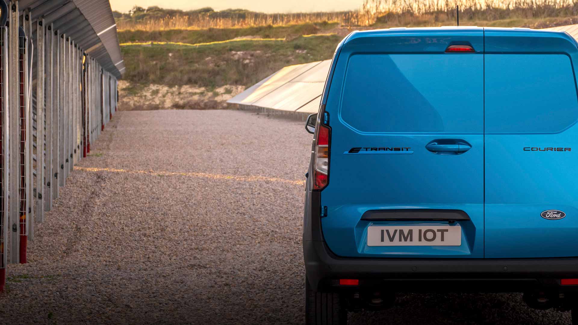 Ford E-Transit Courier in Blau. Heckansicht, fährt auf Schotterweg.