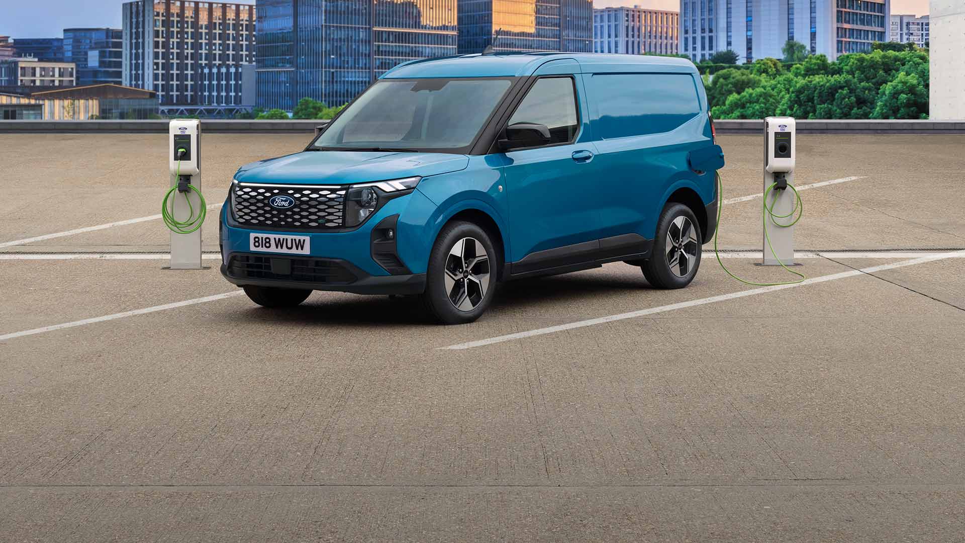 Ford E-Transit Courier in Blau. Dreiviertelansicht, an einer Ladestation angeschlossen mit Hochhäusern im Hintergrund.