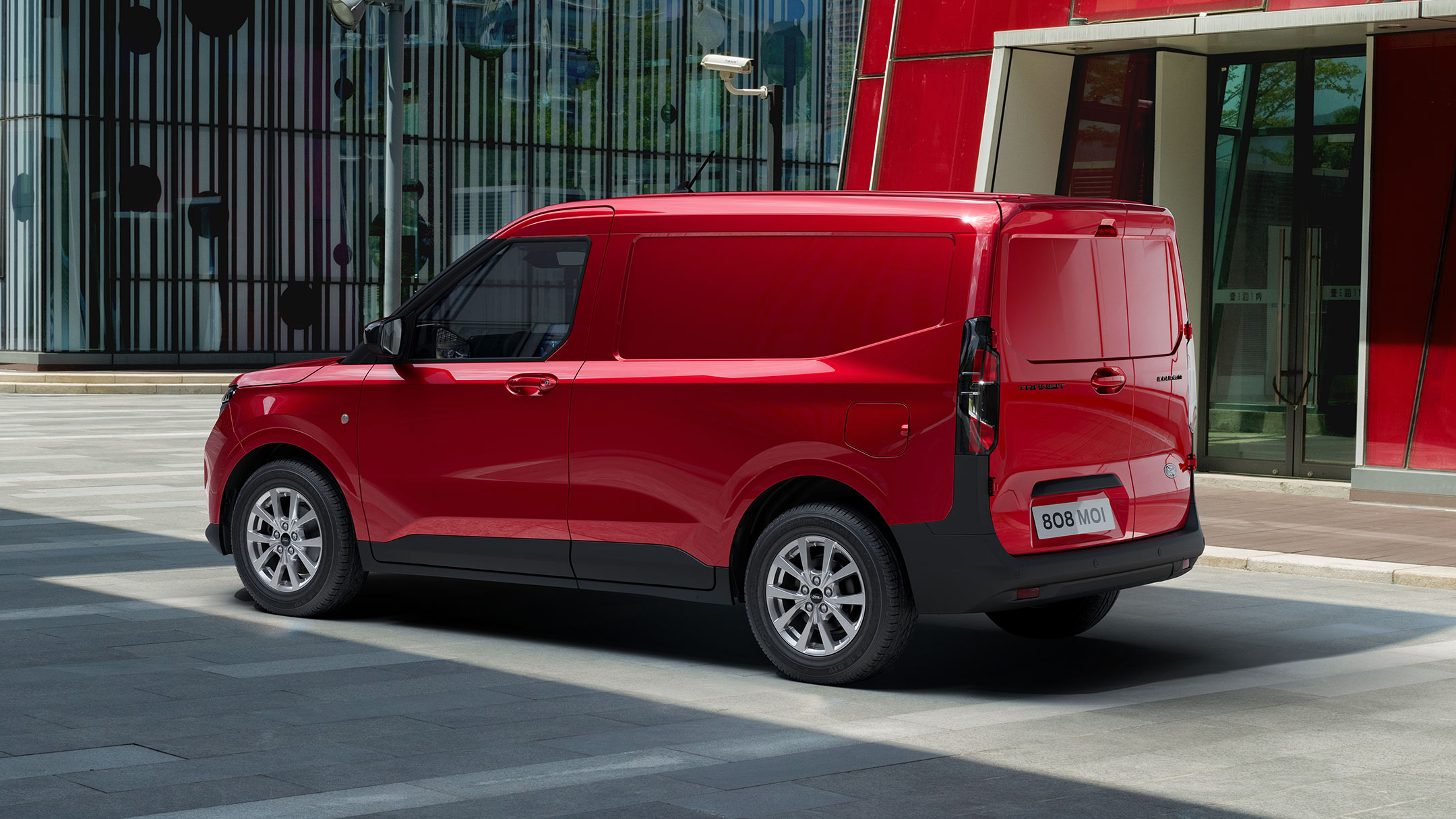 Ford Transit Courier in Rot. Dreiviertelansicht, parkt vor einem Glasgebäude