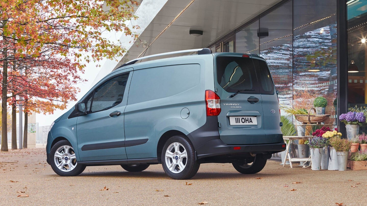 Ford Transit Courier in Blau. Dreiviertelansicht von hinten, parkend vor einem Blumengeschäft 