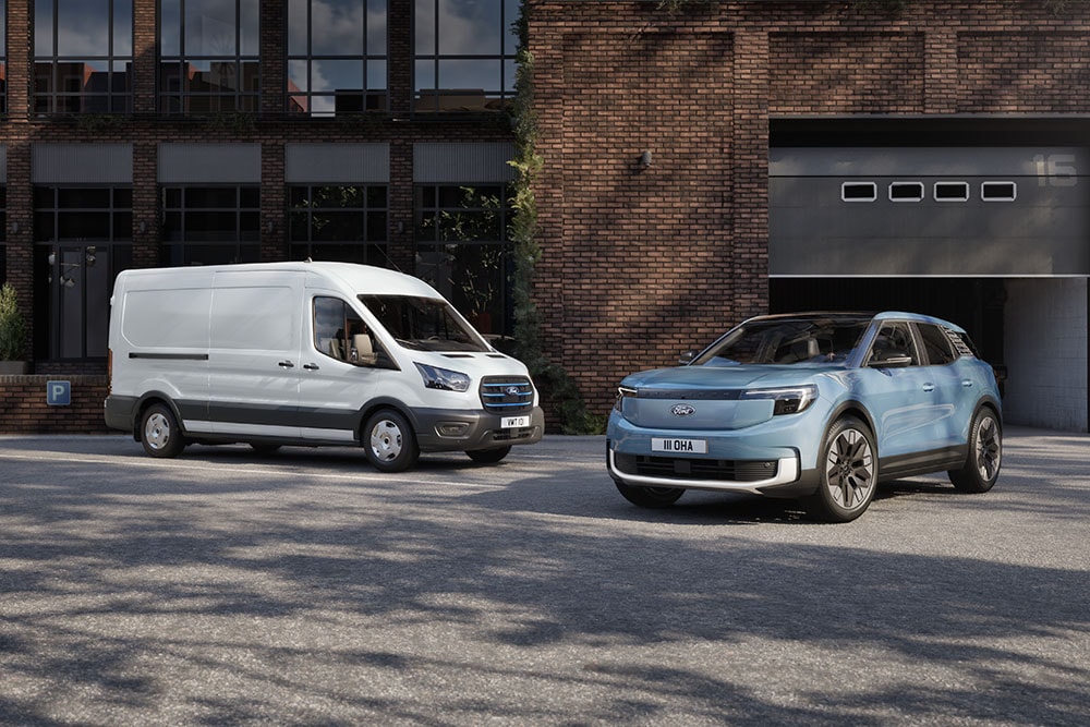 Ford E-Transit in Weiß und ein blauer Ford Explorer parken vor einem modernen Backsteingebäude.