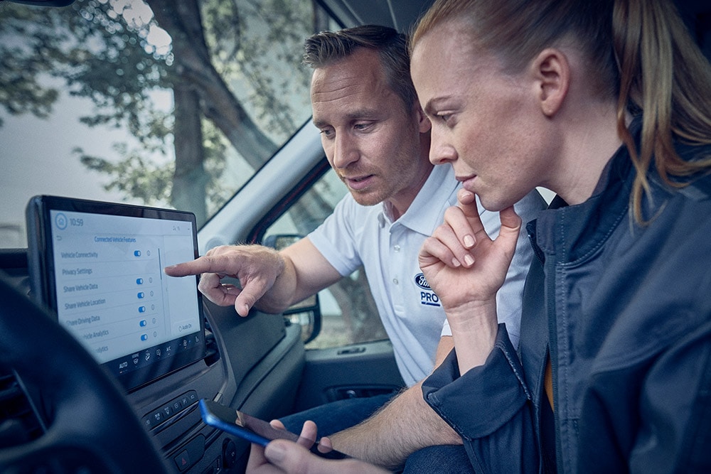 Zwei Personen in einem Ford Fahrzeug, die auf den Touchscreen schauen und etwas besprechen.