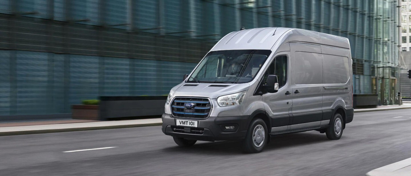 Ford E-Transit in Silber. Dreiviertelansicht, fährt in einer Stadt