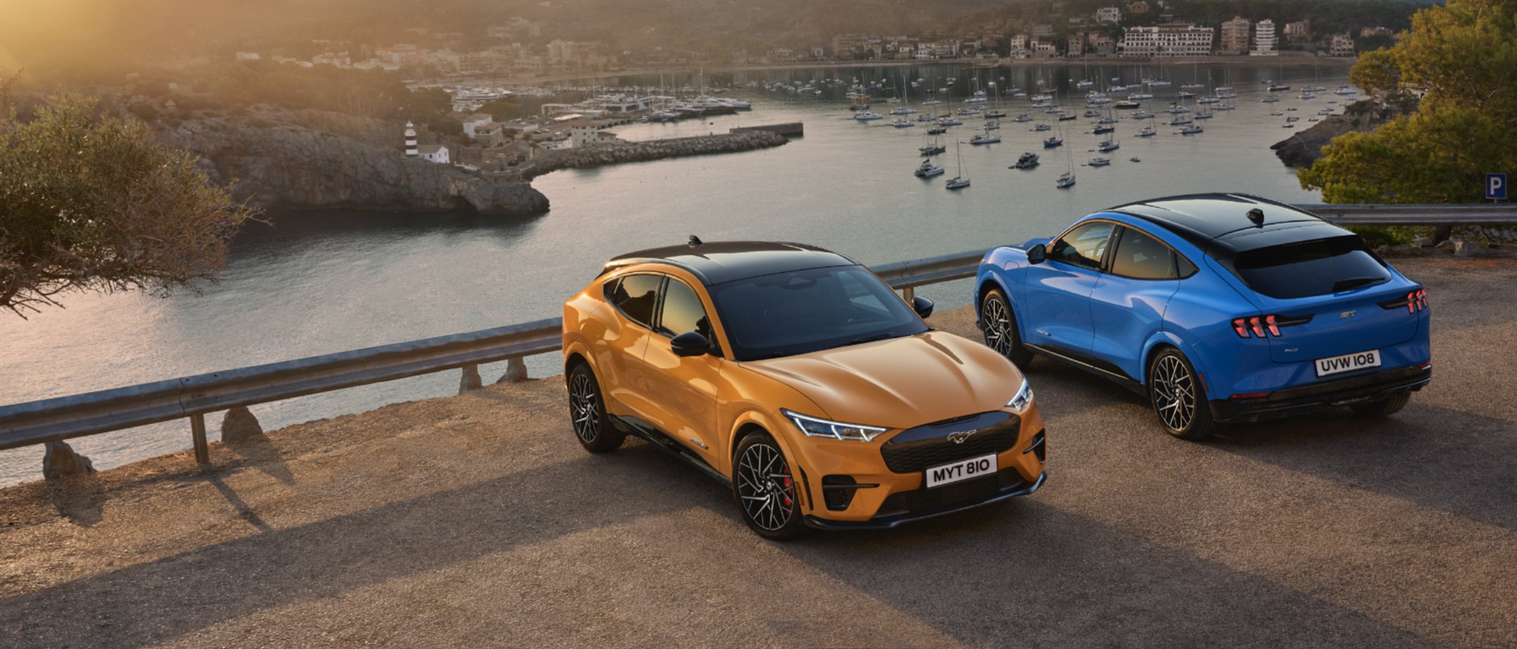 Ford Mustang Mach-E in Orange und Blau. Parken auf einer Aussichtsplattform mit Seeblick