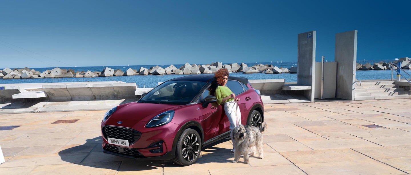 Ford Puma Vivid Ruby Edition. Dreiviertelansicht, mit einer Frau und einem Hund neben dem Fahrzeug