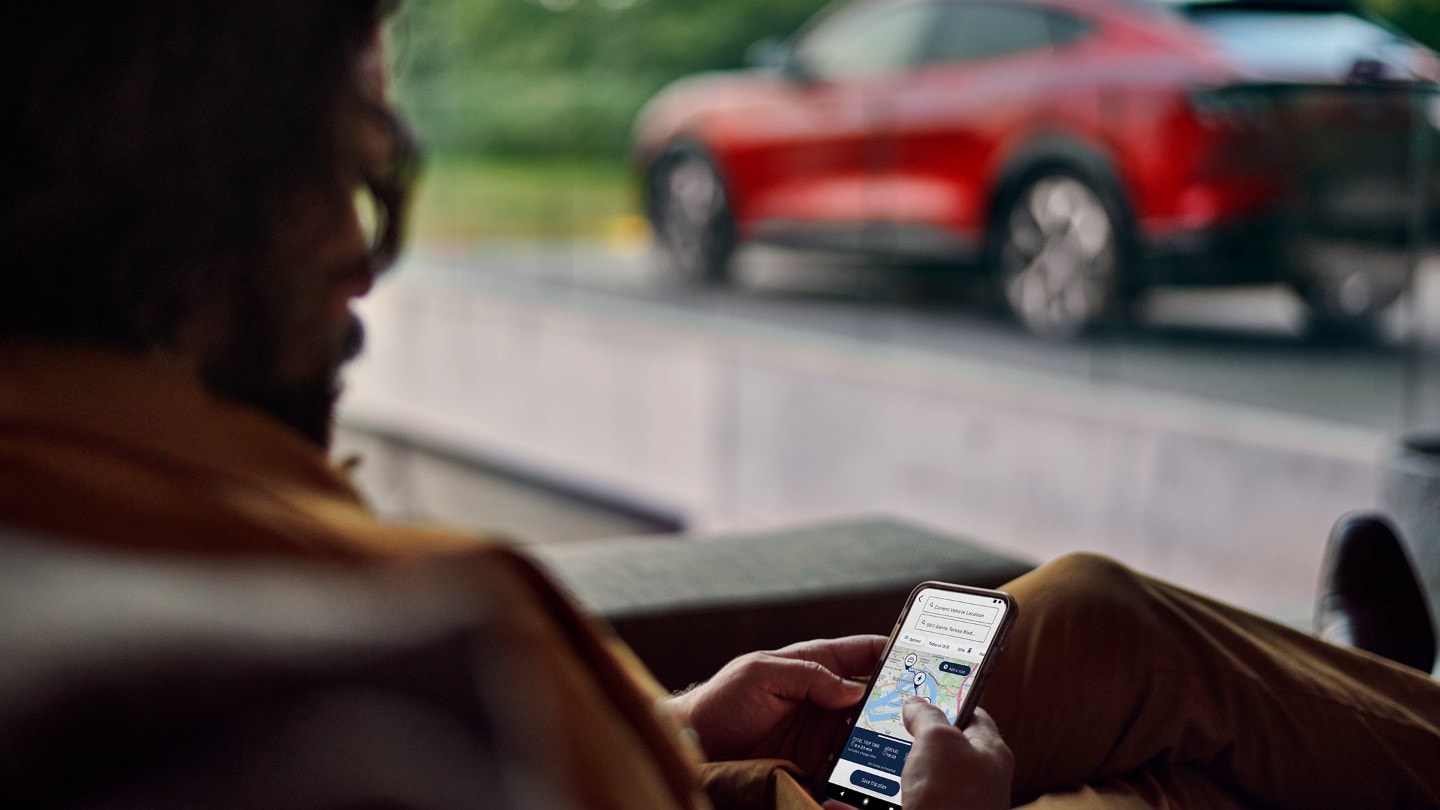 Mann hält Mobiltelefon in der Hand - geöffnete FordPass App mit E-Routenplaner