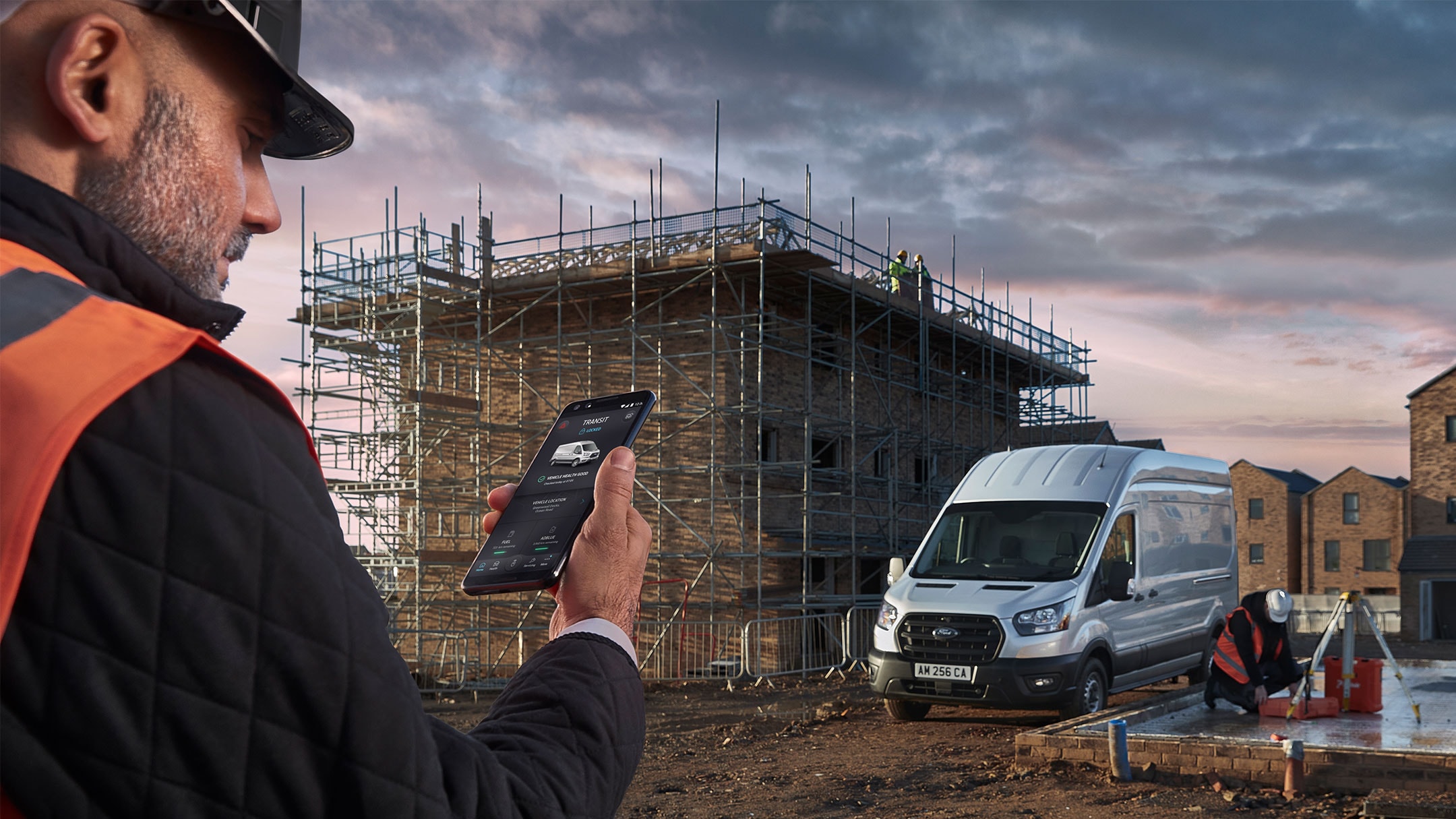 Mann steht auf einer Baustelle und hält ein Mobiltelefon in der Hand 