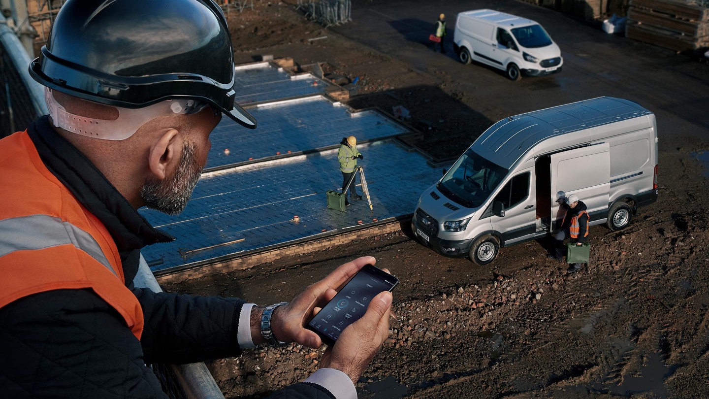 Mann in Warnweste auf einer Baustelle mit Smartphone in der Hand. FordPass Pro App geöffnet