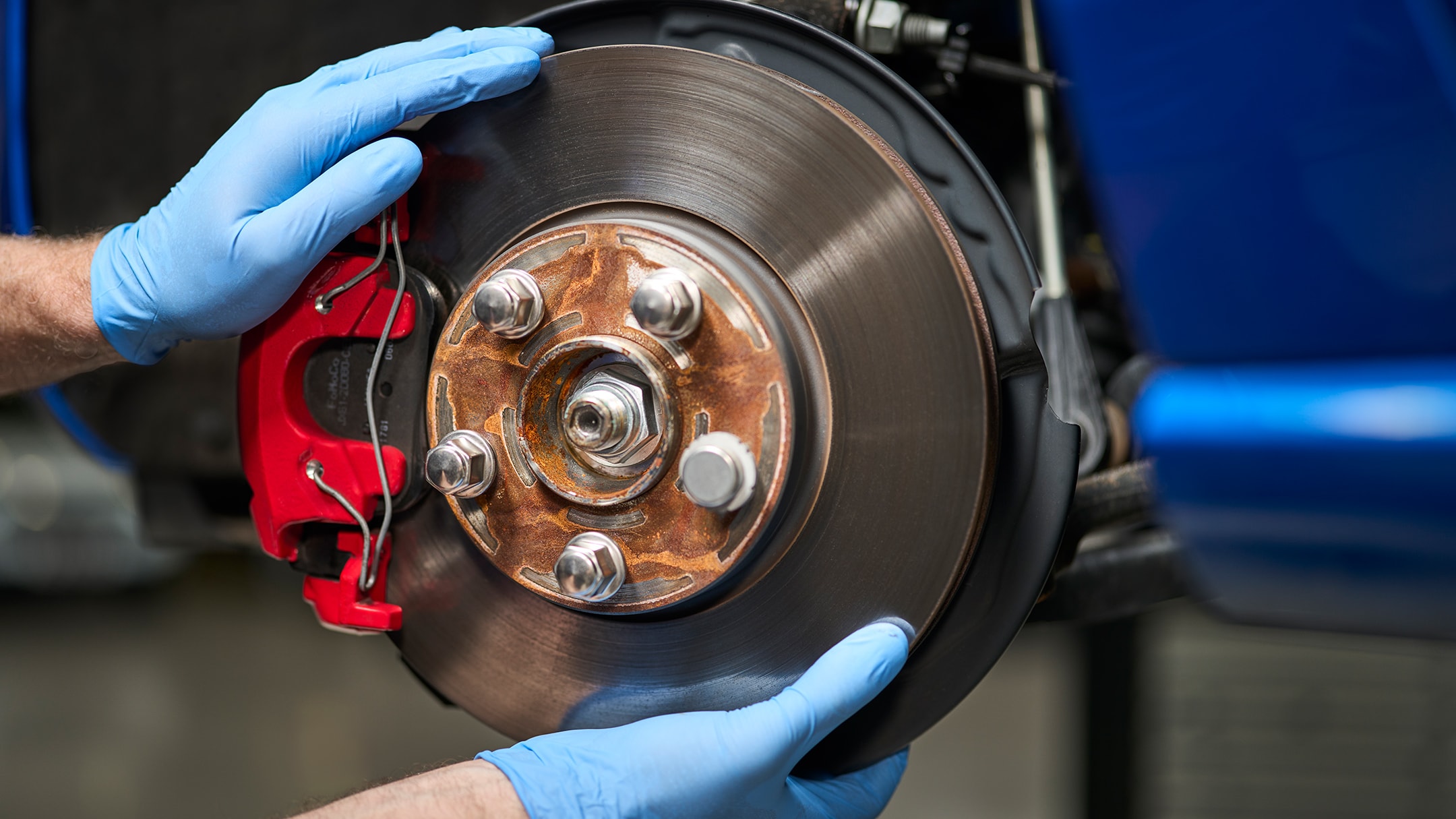 Ein Mechaniker mit blauen Handschuhen montiert eine neue Bremsscheibe an einem blauen Auto.