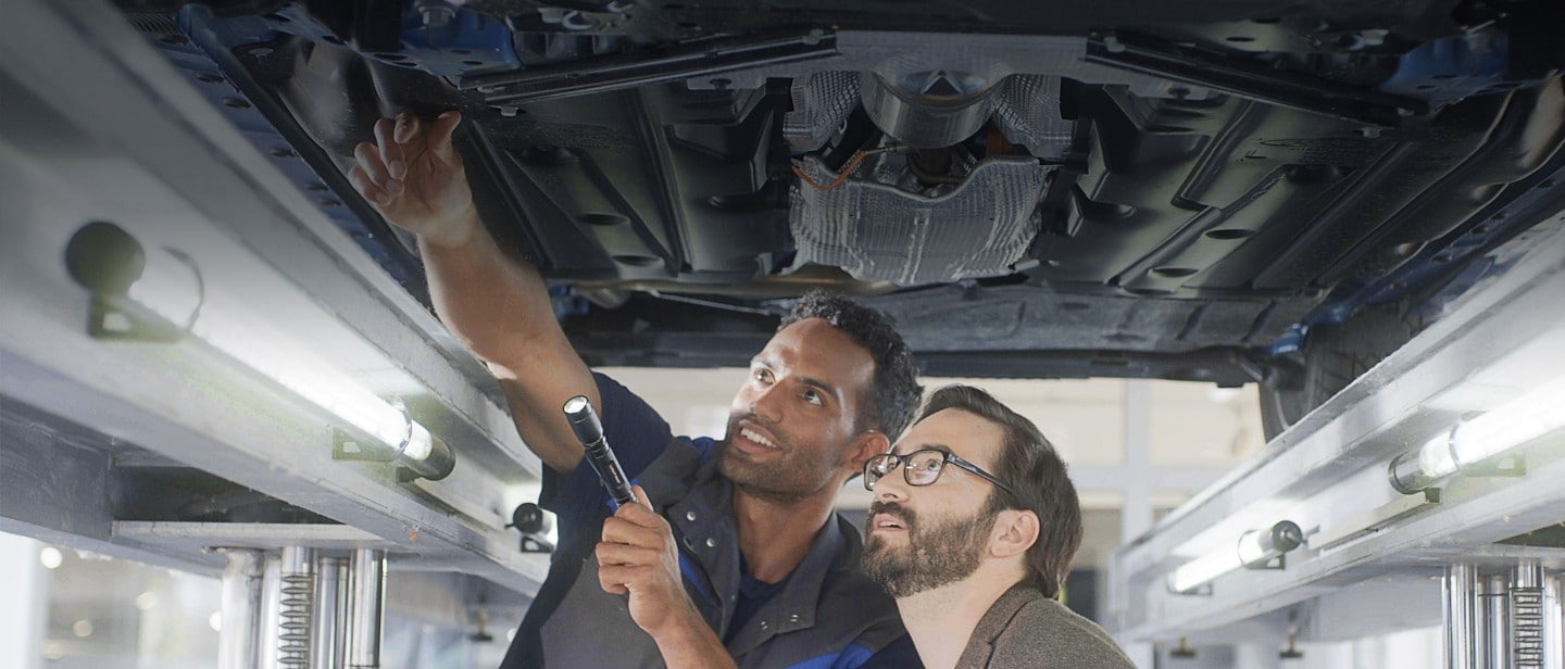 Service employee and customer standing under the car at workshop