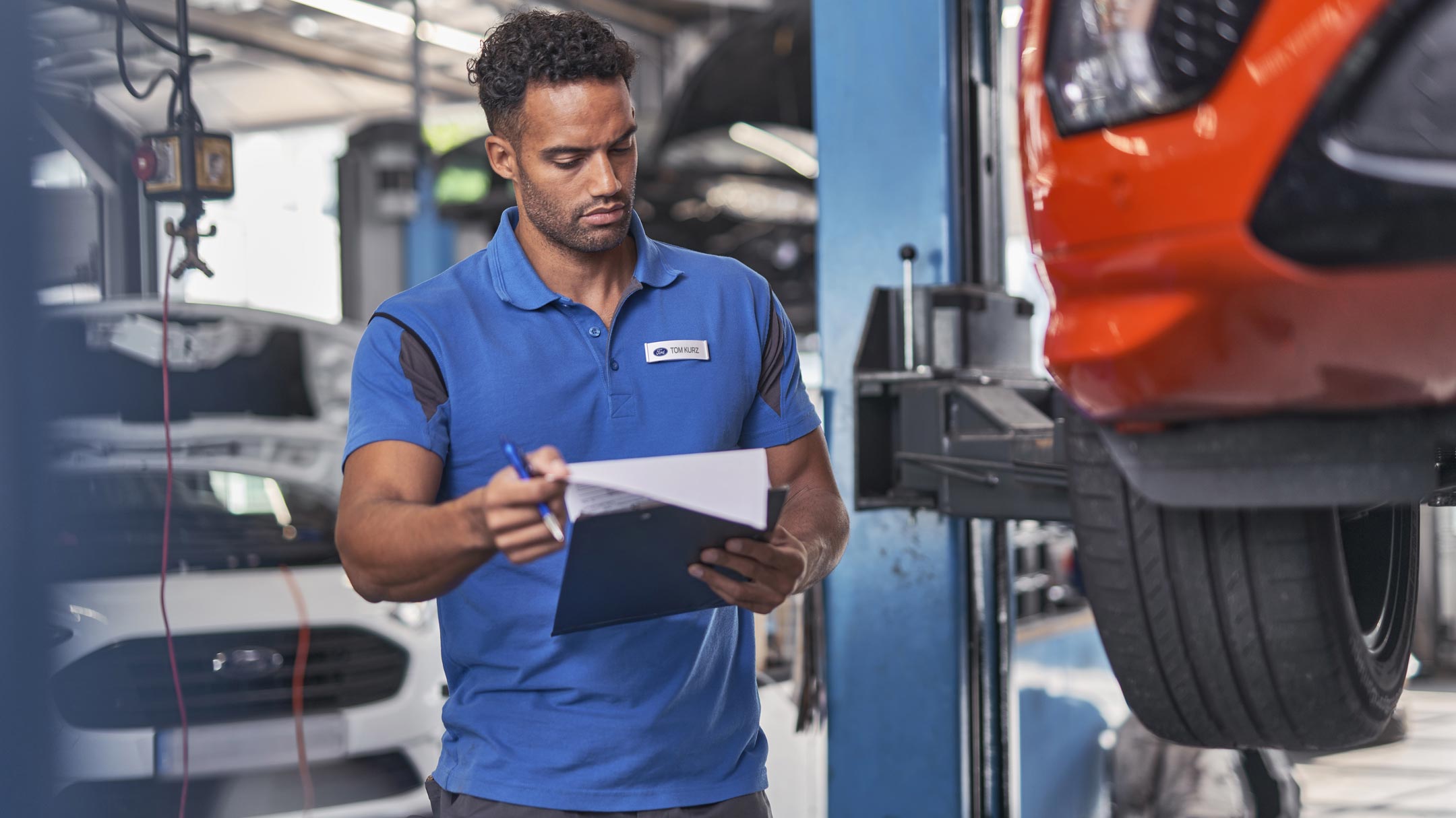A Ford employee shows a tablet to a customer in a showroom with red and blue Ford vehicles.