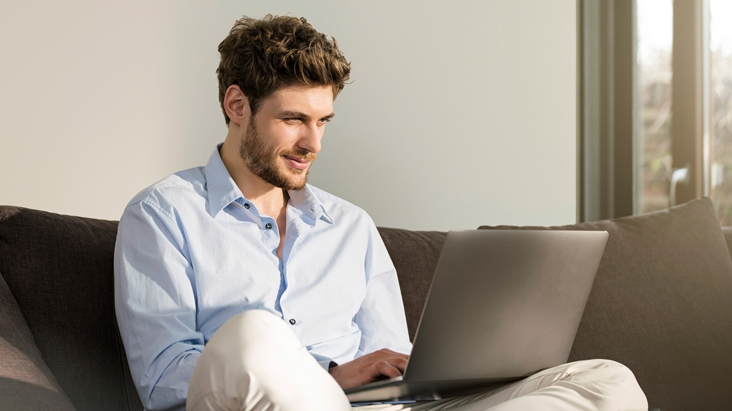 Ein Mann sitzt auf einem Sofa vor einem Laptop