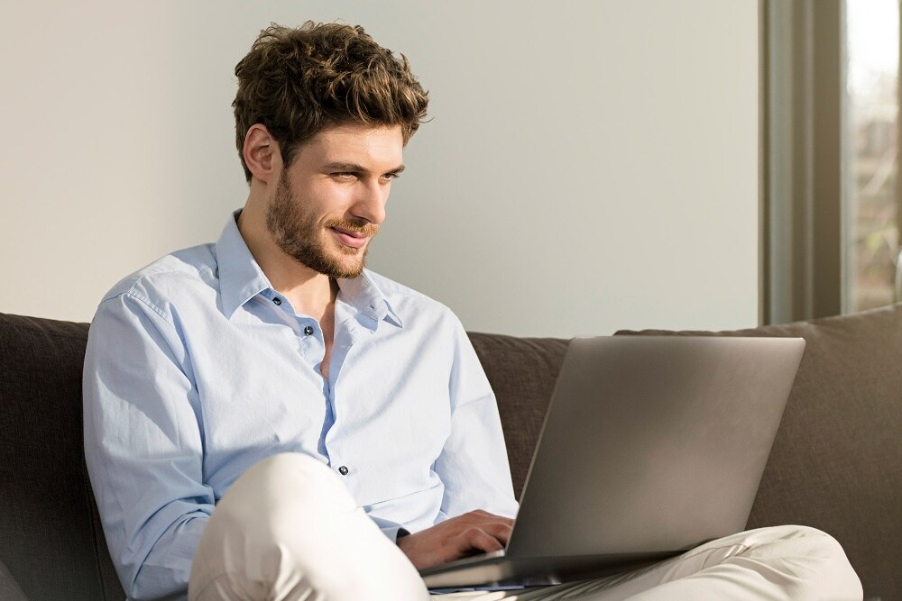 Ein Mann sitzt auf einem Sofa vor einem Laptop