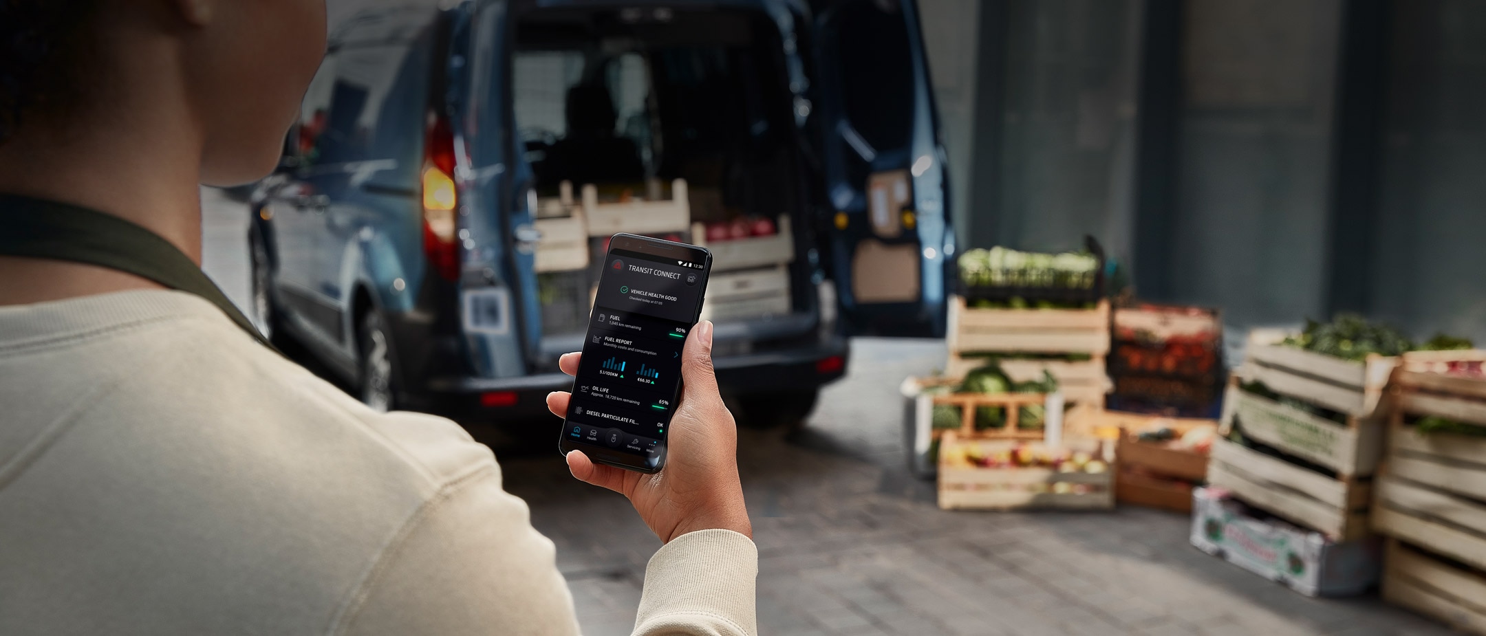 Person steht vor einem Ford Nutzfahrzeug und hält Mobiltelefon mit geöffneter FordPass App in der Hand