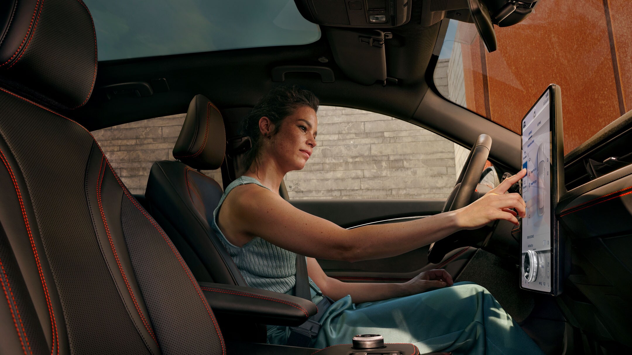 Ford Mustang Mach-E Innenraum. Frau bedient vom Fahrersitz aus den SYNC 4A Touchscreen in ihrem Fahrzeug