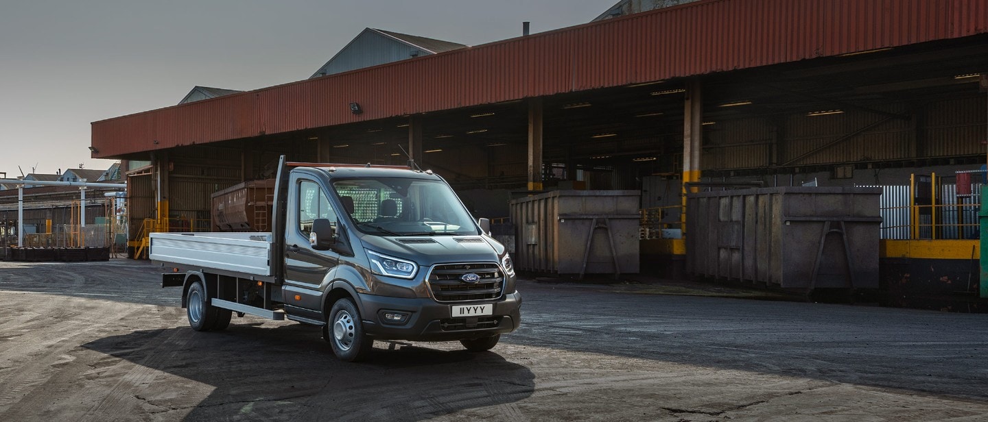 Ford Transit Fahrgestell in Schwarz. Dreiviertelansicht, vor einem Warenlager geparkt