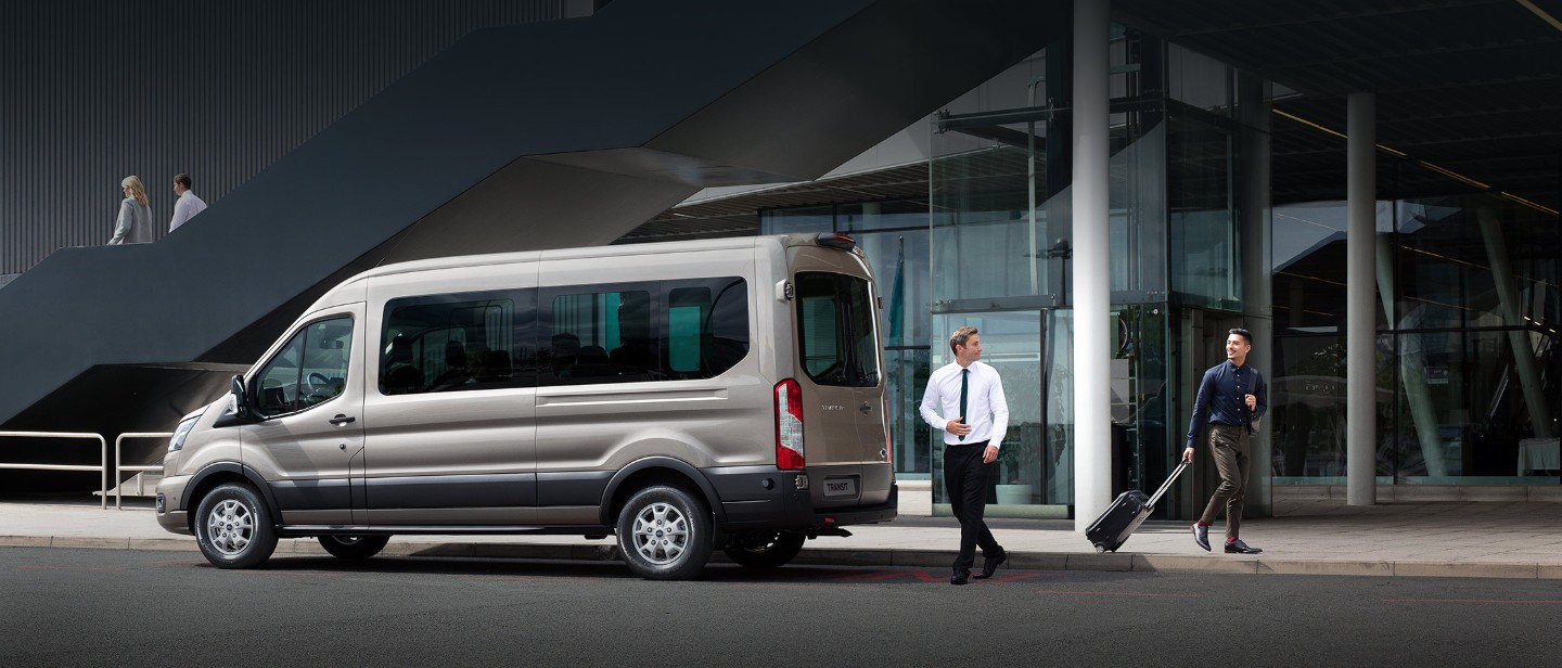 Ford Transit Bus in Silber. Seitenansicht, vor einem Glasgebäude