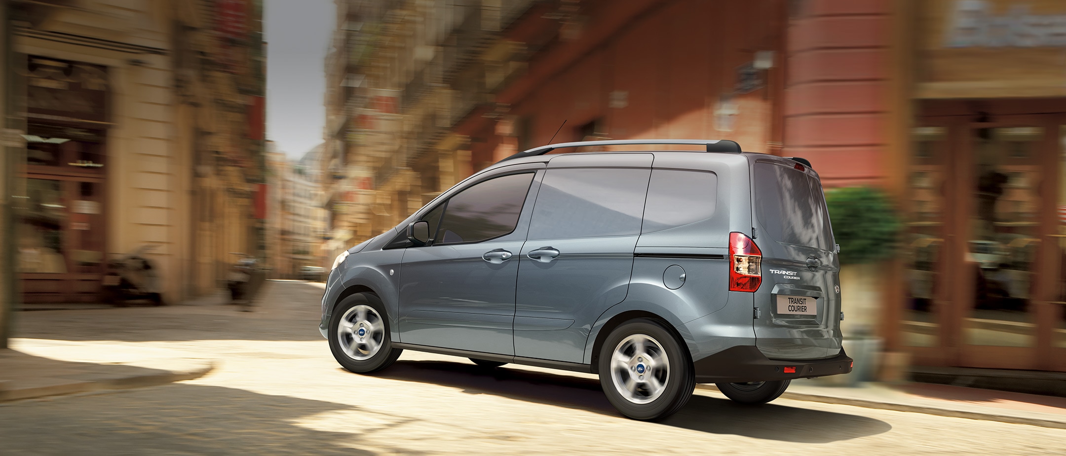 Ford Transit Courier in Blau. Seitenansicht, fährt durch eine Stadt