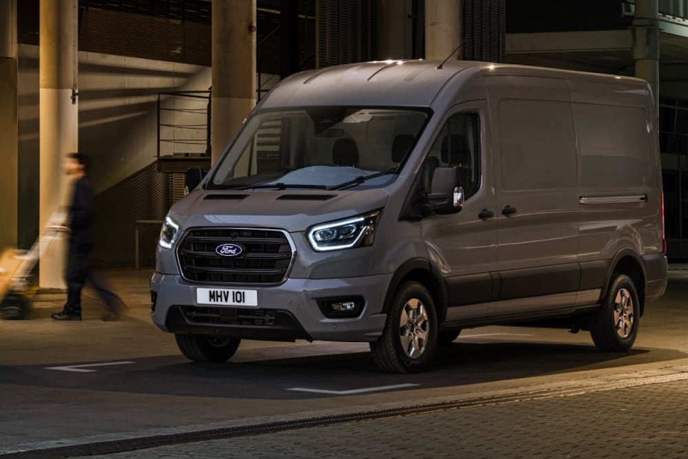 Ford Transit in Grau. Dreiviertelansicht, parkt vor einem Betongebäude.